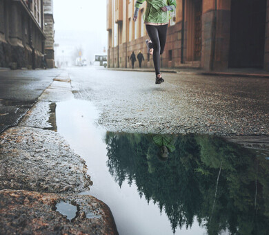 Kvinna springer i stad reflektion av skog i vattenpöl